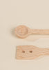 Two wooden utensils from the Wooden Pots and Pans Playset (6 Pcs) rest on a light beige surface: one features a round, spoon-like end, while the other has a flat, angled end with two small holes—ideal additions to any kids kitchen playset or collection of wooden cooking toys.