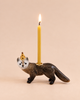 A “Mink Cake Topper - Final Sale” candle holder shaped like a small mink, featuring a yellow keepsake birthday candle on its back and a gold crown on its head, set against a plain beige background.