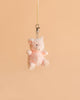 The Bukowski - Baby Oink Pig Bag Charm, a small plush pink piglet keychain, hangs from a beige strap and metal clasp against a plain peach-colored background, making it the perfect plush accessory for your bag.