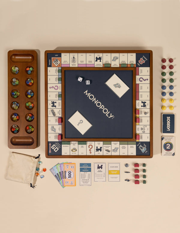 The 3-in-1 Game Collection: Monopoly, Sorry & Mancala features an elegant wooden set with a Monopoly board in the center, cards, money, dice, game pieces, property cards, a cloth bag, and a wooden tray with marbles.