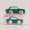 Revamped sentence: A nostalgic toy, the green wooden car—No. 3 GT20 Tommy | Made in England—with “Le Toy Van” on its wheels, sits atop a pink box labeled “GT20 TOMMY,” featuring icons for sustainability, British design, and safety.