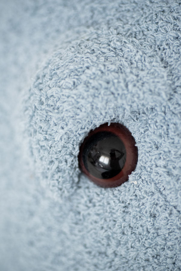 Close-up of a dark brown eye peeking through a hole in a textured blue fabric, featuring an Octopus Stuffed Animal and creating an intriguing and artistic composition.
