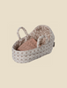 A small, oval-shaped Maileg Carry Cot, Baby with handles, featuring a floral pattern on the exterior and interior lining. Inside the basket is a knitted pink blanket, neatly folded. This versatile carrycot can also double as a portable bunny bed. The background is a plain, light beige color.