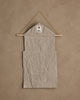 The Coral & Tusk Christmas Clock Advent Calendar is a beige fabric wall hanging with pockets, displayed on a wooden rod and string, featuring a small white tag with a red tree design at the top against a tan textured wall.