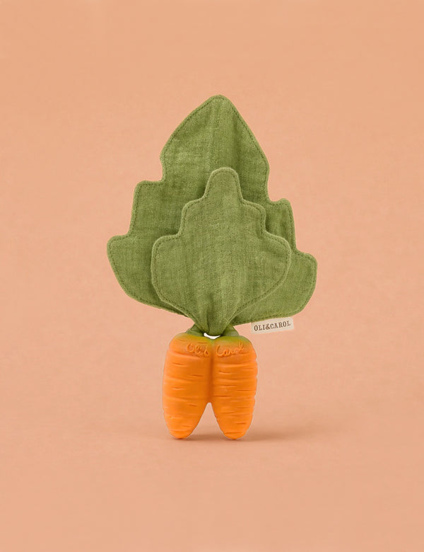 Cathy the Carrot Mini DouDou Teether is a soft toy with two orange roots and green leafy fabric on top—perfect for babies to support sensory development. Shown standing upright against a plain peach background.