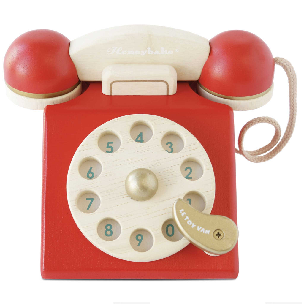 The Vintage Wooden Telephone is a red and beige sustainable toy with a corded handset, number dial (0–9), a small handle labeled “AETOY VAN,” and charming retro-style design.