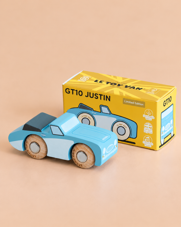 A classic blue wooden car sits in front of a yellow box labeled “No. 1 GT10 Justin | Made in England,” featuring matching car graphics, along with the texts “Le Toy Van” and “Limited Edition.”.