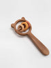 The Sabo Concept Bear and Rings Rattle - Yellow and Pink is a wooden rattle with a bear-shaped frame, handle, and three colorful rings. This charming toy supports motor skills development and is shown on a plain white background.