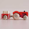 The No. 34 GT190 Tilly, made in England, is a vintage wooden tractor painted in red with natural wood wheels that pulls a matching wooden trailer carrying a small block—an ideal farmyard toy to inspire imaginative play, featured against a plain light background.