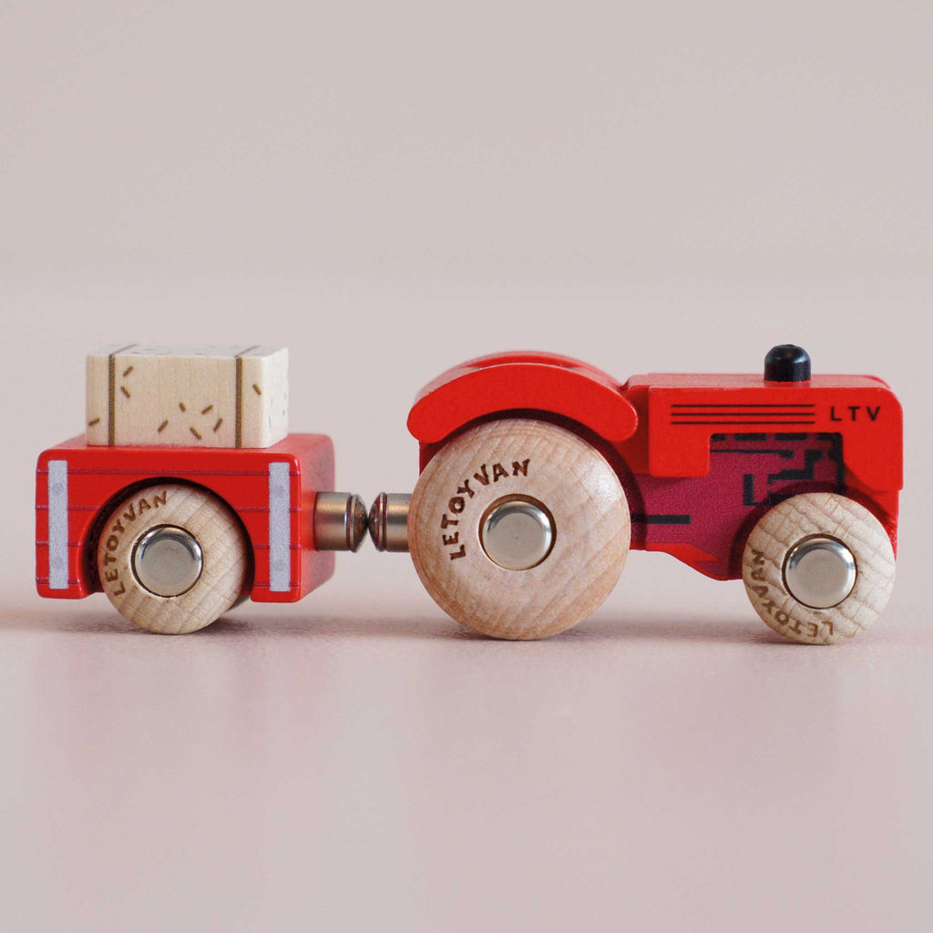 The No. 34 GT190 Tilly, made in England, is a vintage wooden tractor painted in red with natural wood wheels that pulls a matching wooden trailer carrying a small block—an ideal farmyard toy to inspire imaginative play, featured against a plain light background.