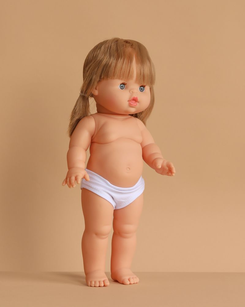 The Minikane Standing Doll (14") - Yze features light skin, straight blonde hair, blue eyes, and white underwear. This anatomically correct doll is made in Spain; clothing is sold separately. The doll stands upright against a beige background.