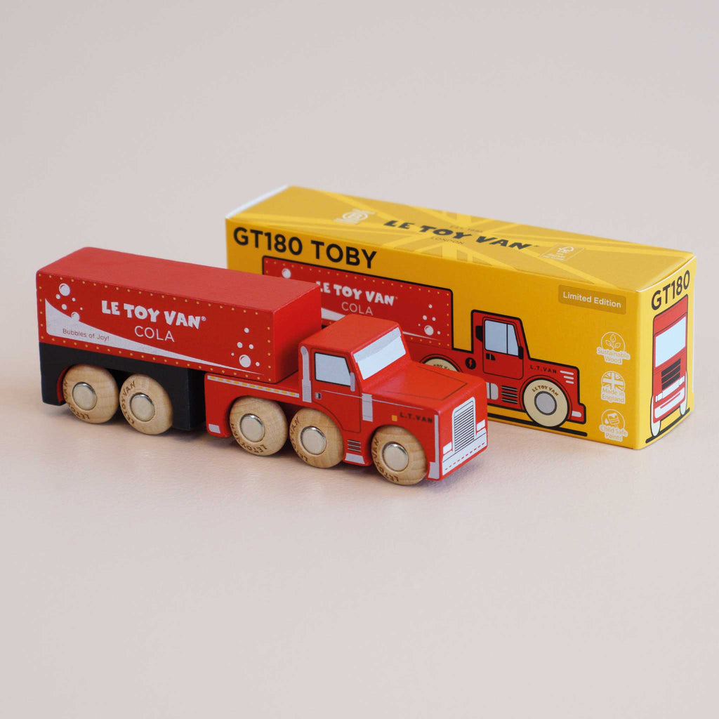 A red wooden truck labeled “No. 33 GT180 Toby | Made in England” is placed in front of its yellow box packaging, which features an illustration of the toy. This vintage-inspired design encourages imaginative storytelling for endless playtime adventures.