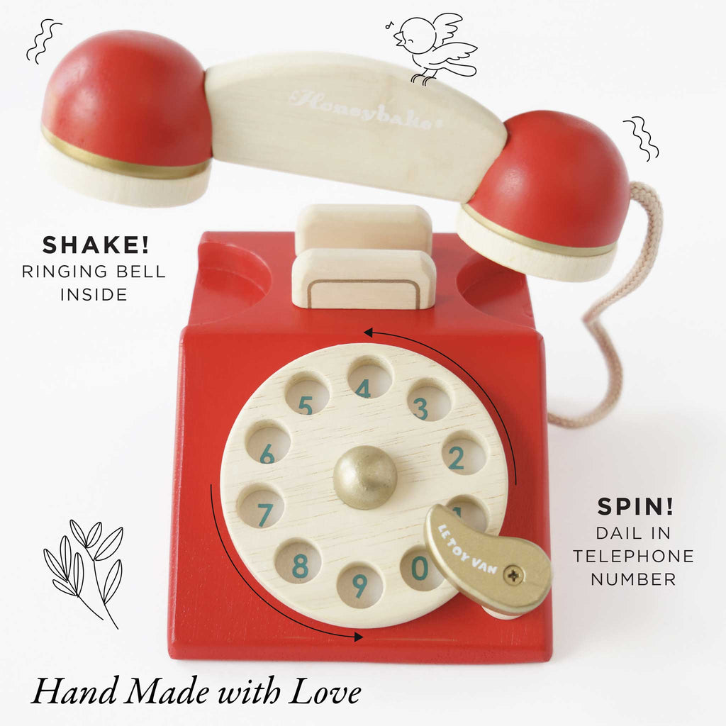 A red and beige Vintage Wooden Telephone, hand made with love. Arrows and text show its ringing bell inside and spinning dial. A small bird illustration appears by the handset of this sustainable wooden toy.