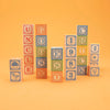 Several Uncle Goose Classic ABC Blocks arranged to form stacks with the word "uncle" highlighted, set against a plain orange background. These educational toys are perfect for learning and fun.