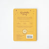 A photo of a yellow book titled "Slumberkins Yak Kin + Lesson Book On Self Acceptance" with star illustrations and text on the cover, promoting self-acceptance and positive self-talk, set against a plain white background.