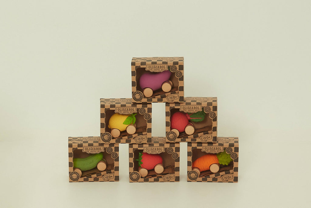 Six FSC-certified wooden boxes, each holding a wheeled veggie toy, are stacked in a pyramid. Visible toys include Betty The Beetroot Baby Car, eggplant, red pepper, yellow pepper, zucchini, radish, and carrot.