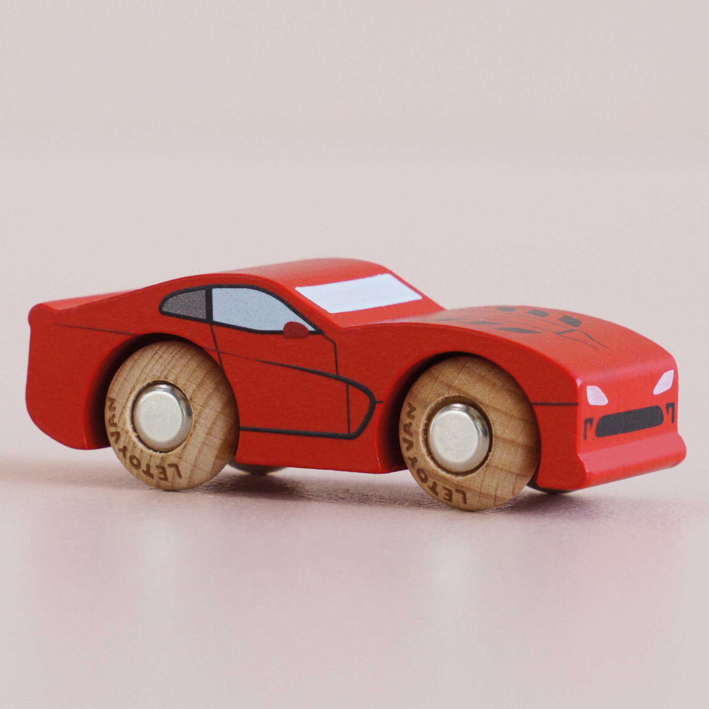 The No. 18 GT100 Jasper, made in England, is a small red wooden toy car featuring black accents and wooden wheels, expertly crafted from sustainable wood to capture the essence of classic performance motoring as it rests on a light surface.