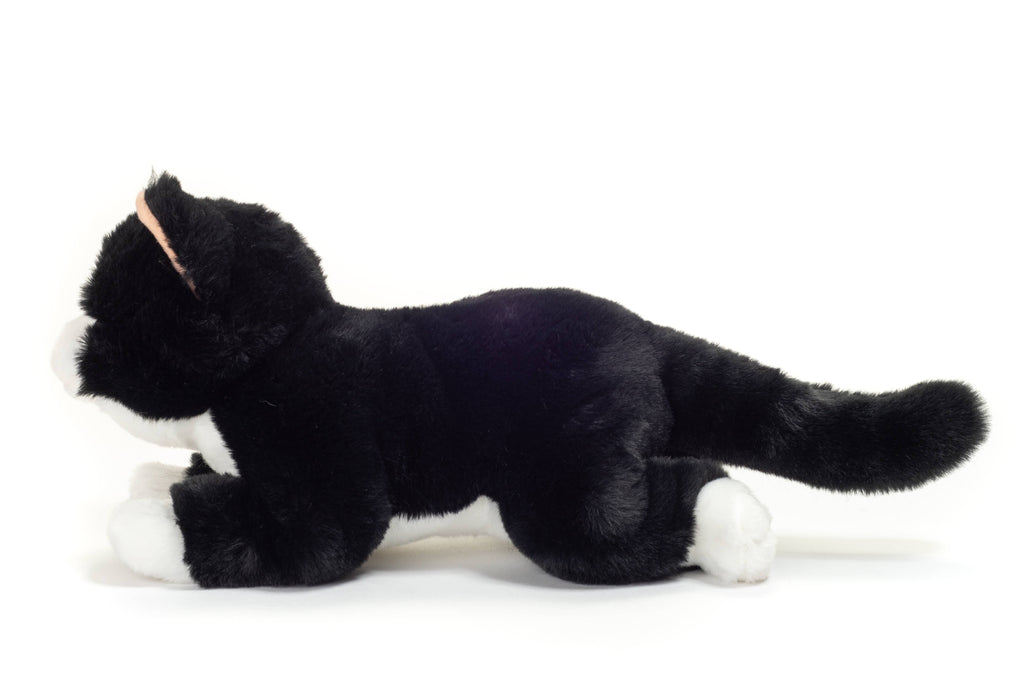 The Teddy Hermann Black Cat Stuffed Animal from the Hermann Teddy Collection showcases a cuddly slouching cat lying on its stomach. This plush black and white feline has a fluffy coat with white paws, chest, and facial accents. Its extended tail adds to its charm against the plain white background.