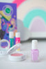A bottle of light purple nail polish from a Klee Naturals Deluxe Makeup Kit - Unicorn Cloud Fairy stands in front of a small makeup compact and two lip balms.