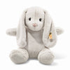 The Steiff Hoppie Bunny Stuffed Animal is a plush, light gray bunny with long floppy ears, black eyes, a pink nose, and a small yellow tag on its left ear—perfect for any plush toy lover.
