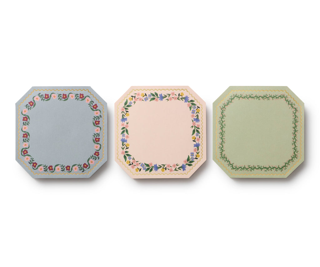 The Gemma Mini Notepad Trio includes three octagonal notepads with decorative floral and leafy borders in blue, pink, and green tones, accented with metallic gold details, displayed side by side against a white background.