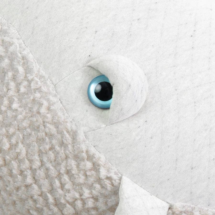 The image shows a close-up of BigStuffed's The Big Whale Albino stuffed animal, featuring a textured fabric surface with a cream and light gray color scheme. A large, bright blue eye surrounded by white hints at exciting ocean adventures.