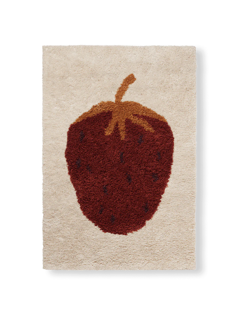 A Ferm Living Fruiticana Tufted Strawberry Rug featuring a large, stylized depiction of a strawberry in deep red with a brown stem, set against a cream background. The design is simple yet bold, focusing on the