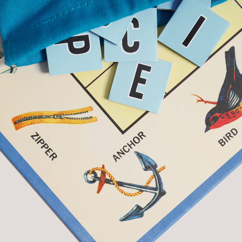 A Scrabble for Juniors Vintage Bookshelf Edition game board featuring illustrations of a zipper, an anchor, and a bird, with letter tiles spelling “PIECE” placed above the anchor.