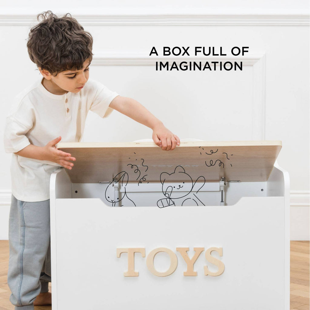 A young boy opens a hand-crafted Toy Storage Box labeled "TOYS," revealing playful illustrations of stuffed animals inside. Text on the wall reads, "A BOX FULL OF IMAGINATION.