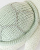 Close-up of the Cuddle + Kind Baby Sea Turtle (Kelp Green), a soft, hand-knit toy featuring a textured shell with gray stitching and part of its flipper—a charming, heirloom-quality piece.