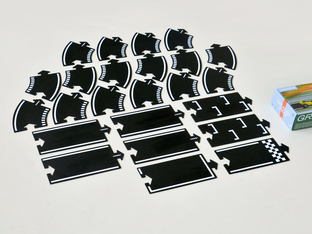 The Large Flexible Toy Race Track - Grand Prix features black plastic track pieces—straight, curved, and finish line sections—arranged in rows on a light surface beside the partially visible product box.