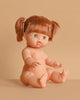 The Minikane Baby Doll (13") - Gabrielle, featuring light skin, green eyes, and brown pigtails, sits on a beige surface with a matching beige background. (Clothing sold separately.).