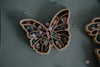 A wooden butterfly-shaped tray holds an array of flower- and butterfly-shaped creations, all crafted with the Fairy Cutter Set - Eco Playdough Tool, and rests on a gray surface—perfect for inspiring sensory play.