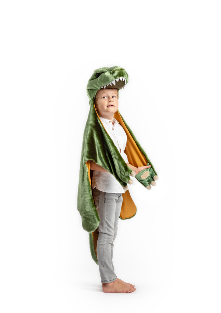 A young child stands barefoot in a green Costume - T-Rex Dino with a dinosaur head hood, wearing a white shirt and light gray pants, looking slightly upward against a white background.