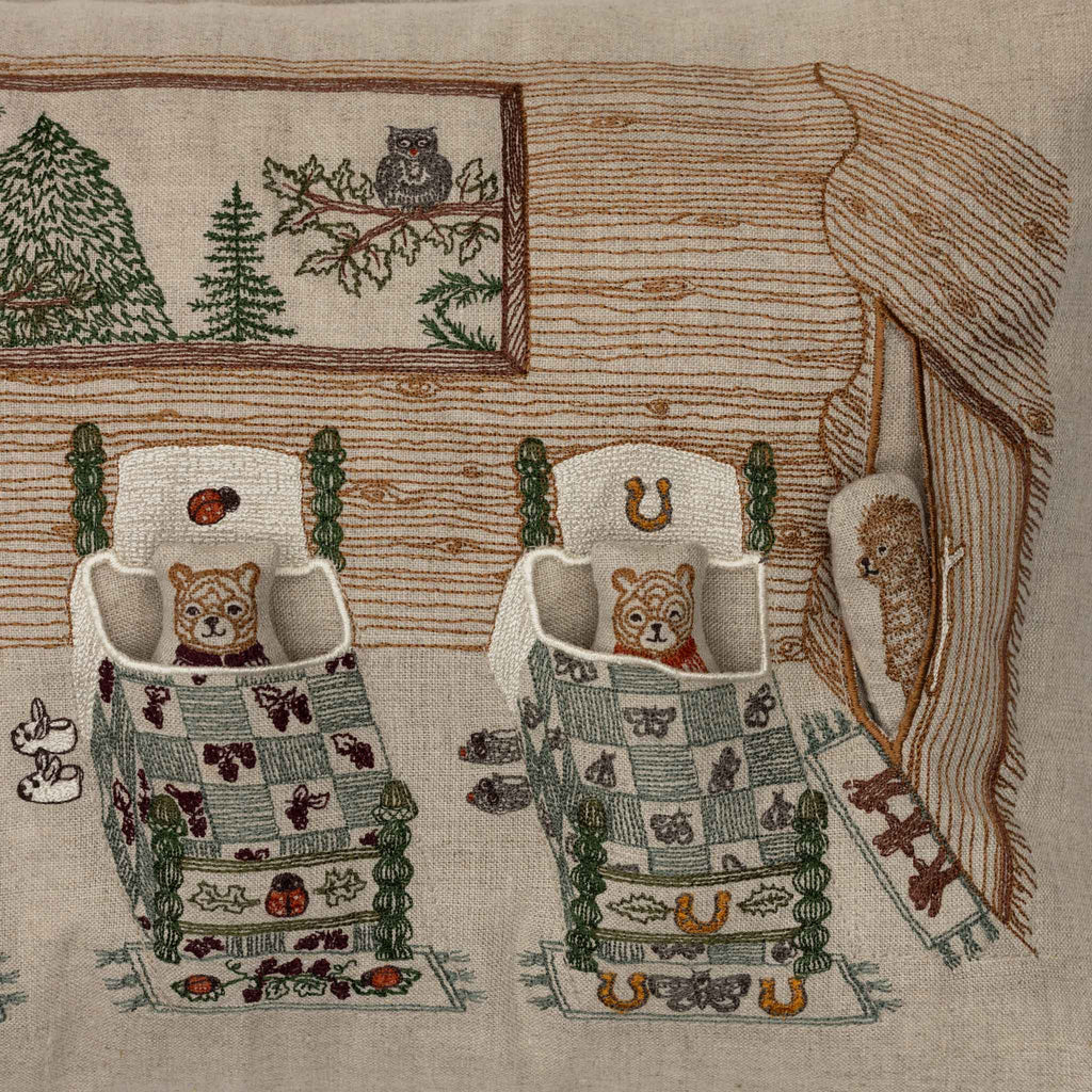 The Coral & Tusk Three Little Bears Pocket Pillow features an embroidered log cabin scene with two beds holding bear cubs, patterned blankets, a window with an owl, beehive by the door, and horseshoes. Ships in one week.