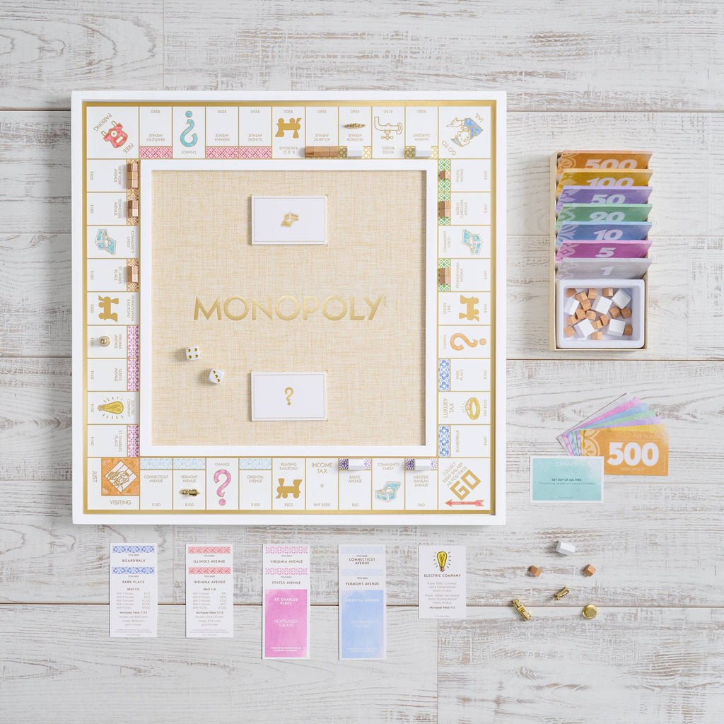 A gold foil-stamped Monopoly Bianco Edition game board with gold-toned spaces and center logo, accompanied by stacks of multicolored paper money, wooden building tokens, property cards, and two dice on a light wooden surface.