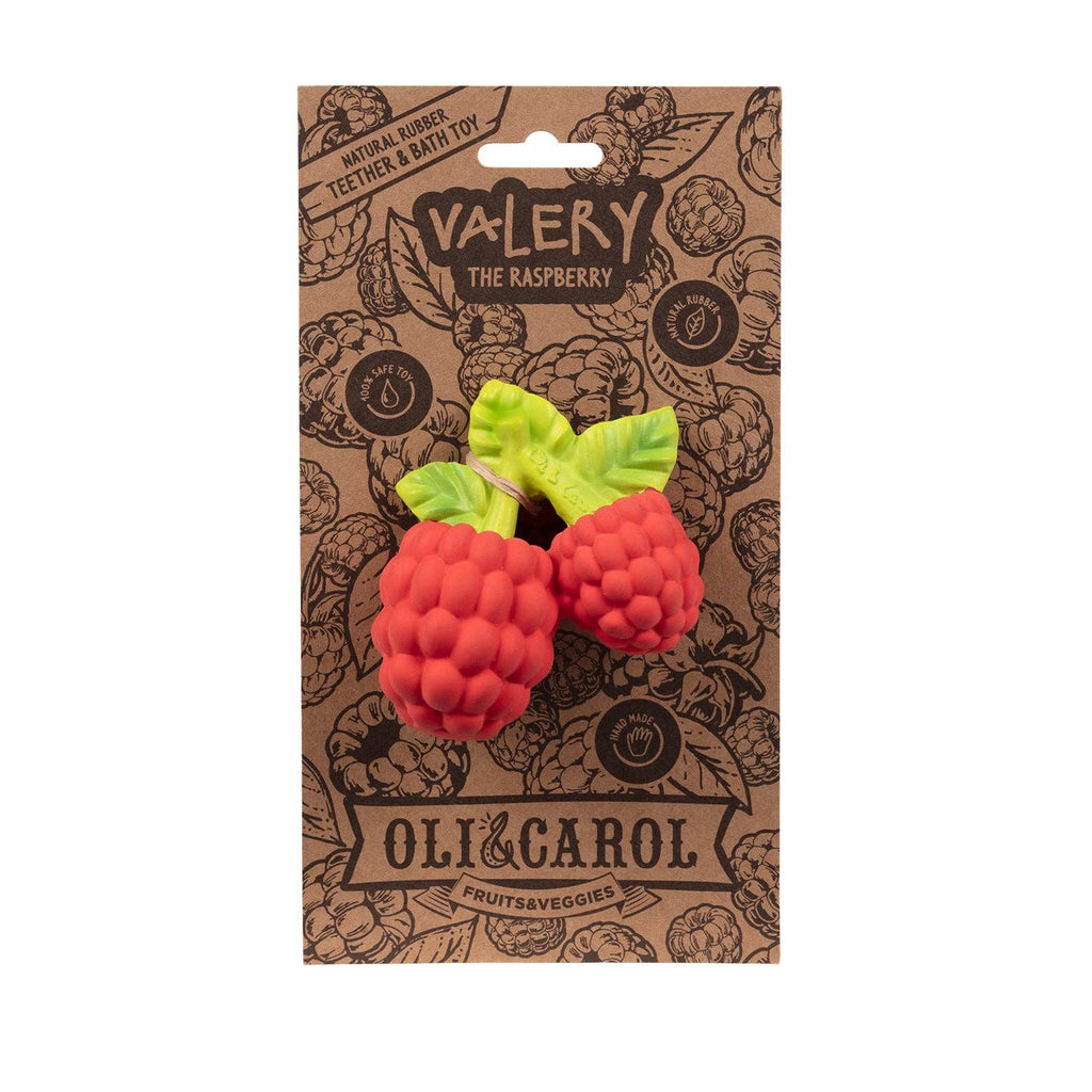 The Valery the Raspberry Teething Toy, shaped like two red raspberries with green leaves, is an eco-friendly sensory teether made from natural rubber and sold on a fruit-themed cardboard backing labeled “Oli & Carol.”.