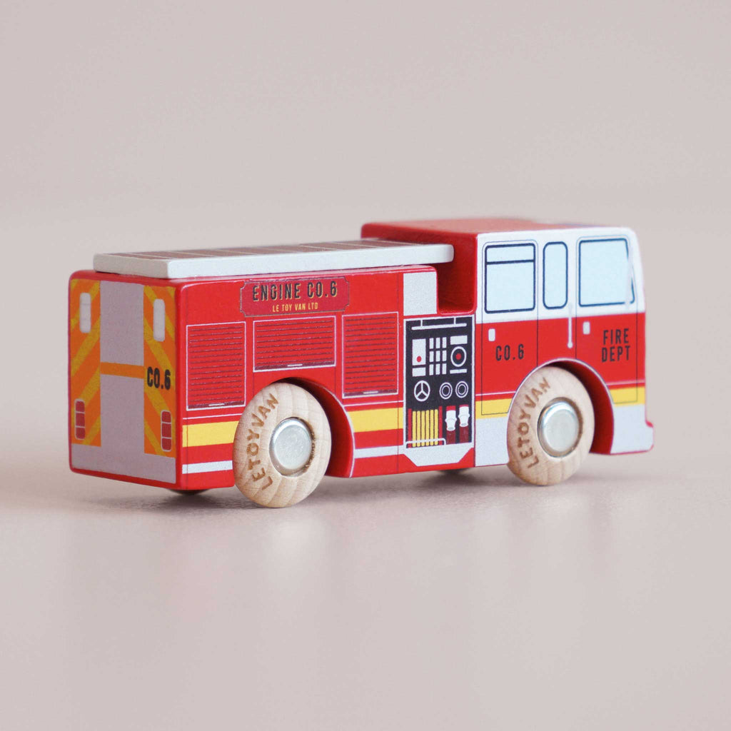 A small wooden fire engine toy—No. 44 GT270 Quinn, made in England—painted red with yellow and white details and labeled “FIRE DEPT” and “ENGINE CO.6,” sits on a light surface. Perfect for imaginative adventures, its wooden wheels bear the printed name “LeftyVan” and are ready to roll into playful rescue missions.