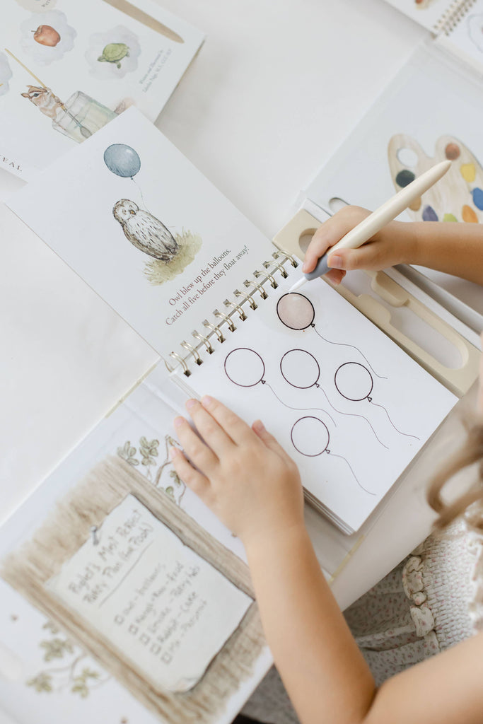 A child uses a water pen to color a balloon on a spiral-bound Winnie-the-Pooh: Pooh’s Birthday Surprise (Water Reveal) book, which features a watercolor illustration of an owl.