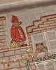 Coral & Tusk Holiday House Advent Calendar featuring embroidered linen with a bear in a winter coat standing on a brick wall next to a house where a second bear peers out of a window.