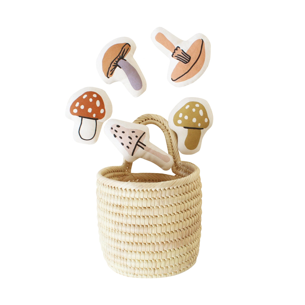 A hand-woven Mini Mushroom Basket with wooden play pieces shaped like mushrooms and an ax, all against a white background.