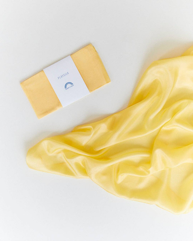 Sarah's Silks Solid Color Playsilk - Sunshine is a folded yellow cloth with a white label next to a shiny, loosely spread playsilk on a white surface—perfect for open-ended play and inspired by Waldorf toys.