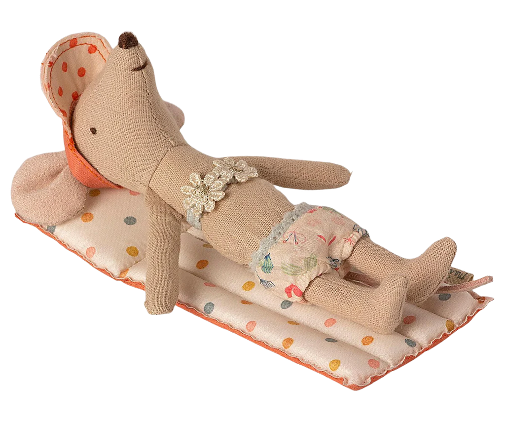 The Maileg Beach Float, Mouse - Multi Dot is lounging on a polka-dotted cushion, resembling an air mattress. This cute mouse is dressed in floral-patterned shorts and a headscarf adorned with red polka dots. It looks completely relaxed, lying on its back with its arms by its sides and feet stretched out.