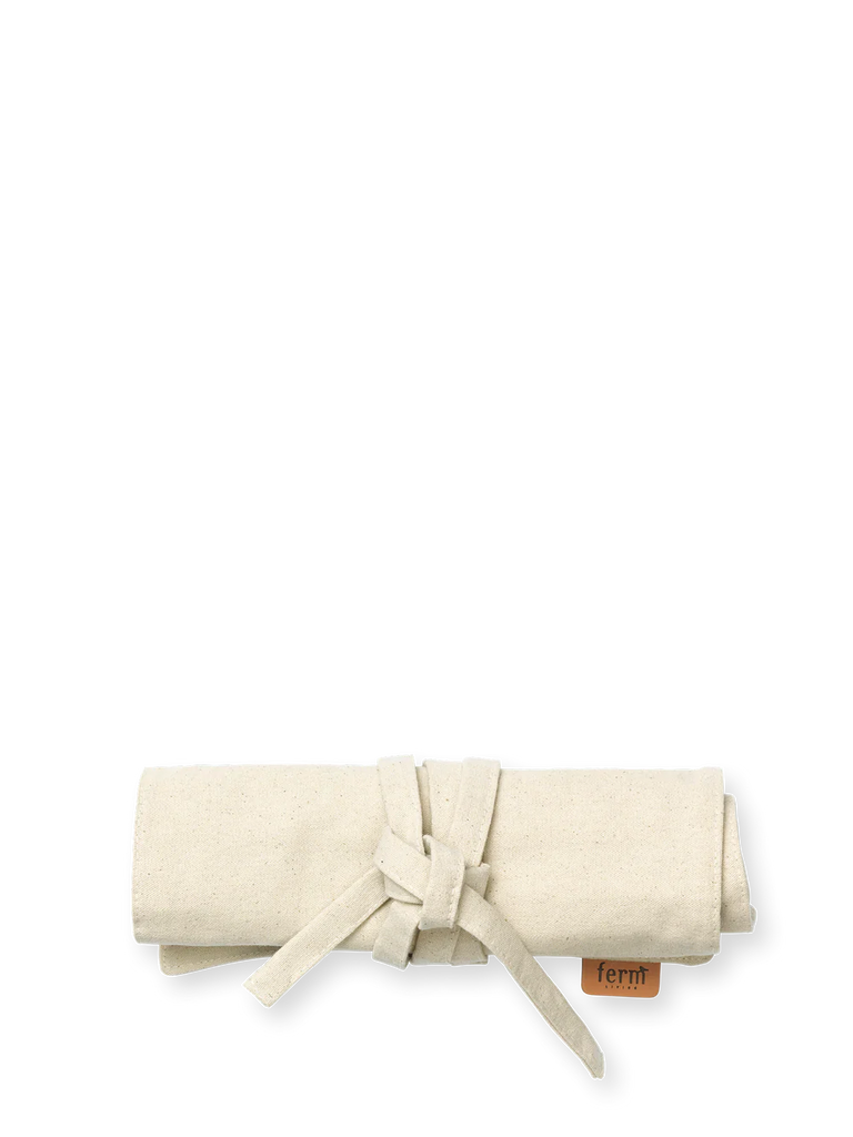 The Ferm Living Ally Pencil Wrap in off-white, crafted from organic cotton with a tan tag, is neatly rolled and tied, shown on a plain white background.