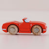 A small No. 13 GT75 Marc wooden toy car, made in England, is displayed in profile on a light surface and background, featuring a racing red finish and natural wood wheels.