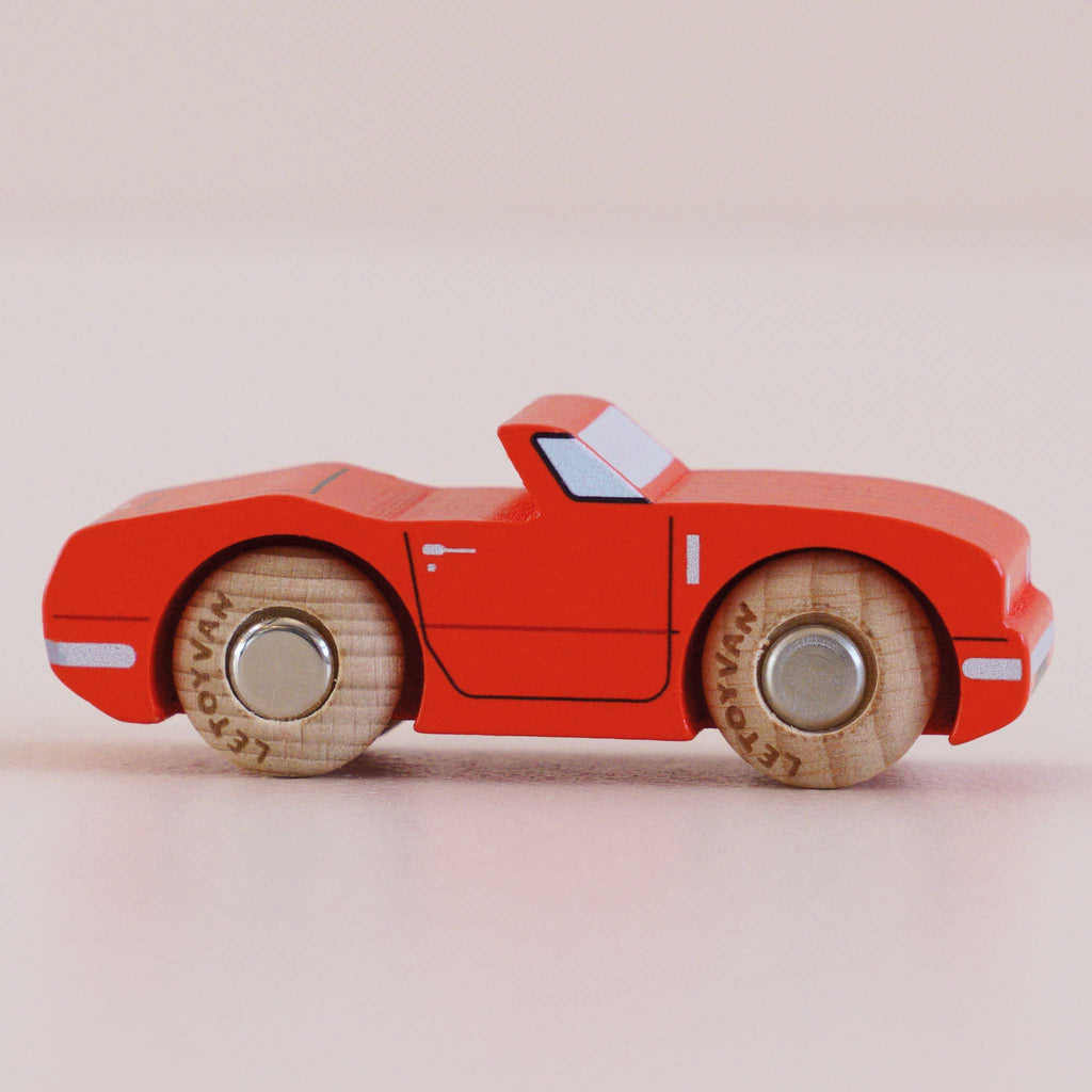 A small No. 13 GT75 Marc wooden toy car, made in England, is displayed in profile on a light surface and background, featuring a racing red finish and natural wood wheels.