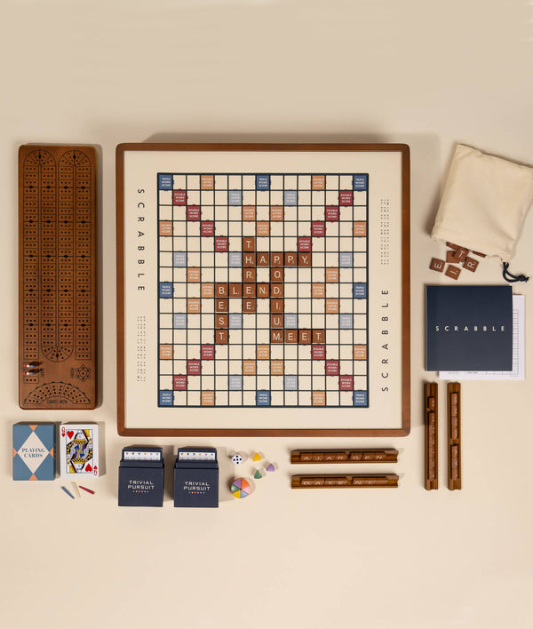 The 3-in-1 Game Collection: Scrabble, Trivial Pursuit & Cribbage features Scrabble with words like “HAPPY,” “BLEND,” and “MEET” on the board, plus a cribbage board, racks, tiles, cards, dice, scorepad, bag, and Trivial Pursuit trivia cards.