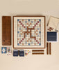 The 3-in-1 Game Collection: Scrabble, Trivial Pursuit & Cribbage features Scrabble with words like “HAPPY,” “BLEND,” and “MEET” on the board, plus a cribbage board, racks, tiles, cards, dice, scorepad, bag, and Trivial Pursuit trivia cards.