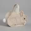 An Easter basket in the shape of a Coral & Tusk Bunny Basket, made of soft fabric, featuring detailed stitching to depict the rabbit's fur and features, complemented by a fluffy white pom-pom tail.