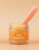 A small jar of "Tiny Tummies- Banana Jelly food - Tiny Harlow" comes with a magic spoon nestled inside, perfectly designed for doll meals. The label showcases an adorable banana graphic set against a cozy warm beige background.